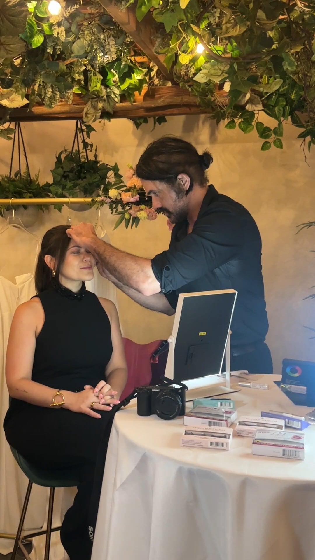 Glamsquad makeup artist working at a flower-decorated event station