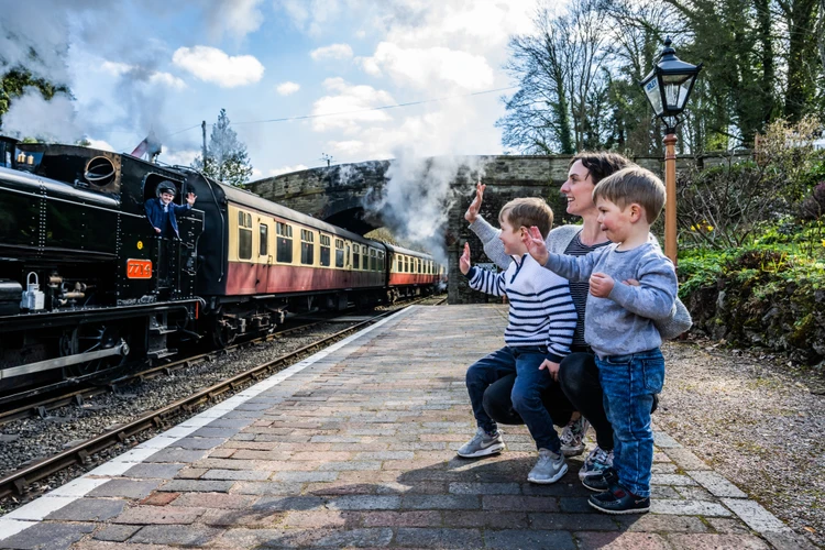 A parent and children wave to a heritage railway conductor