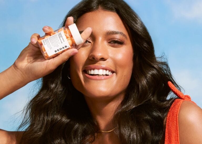 Model holding a REHAB Your Hair capsule bottle