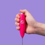 A hand uses the pink Spacegoods frother to mix a drink
