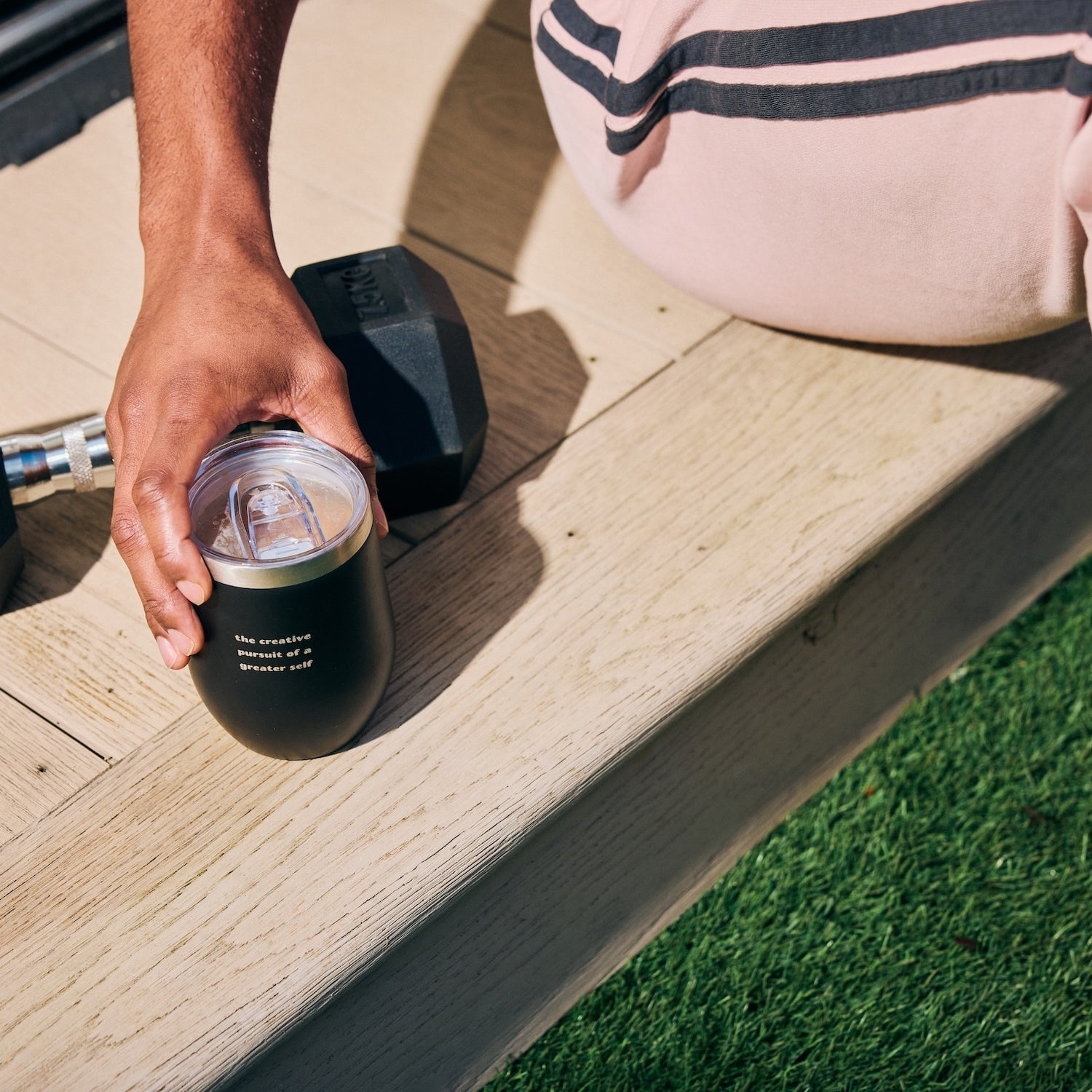 Person holding a drink beside outdoor exercise equipment